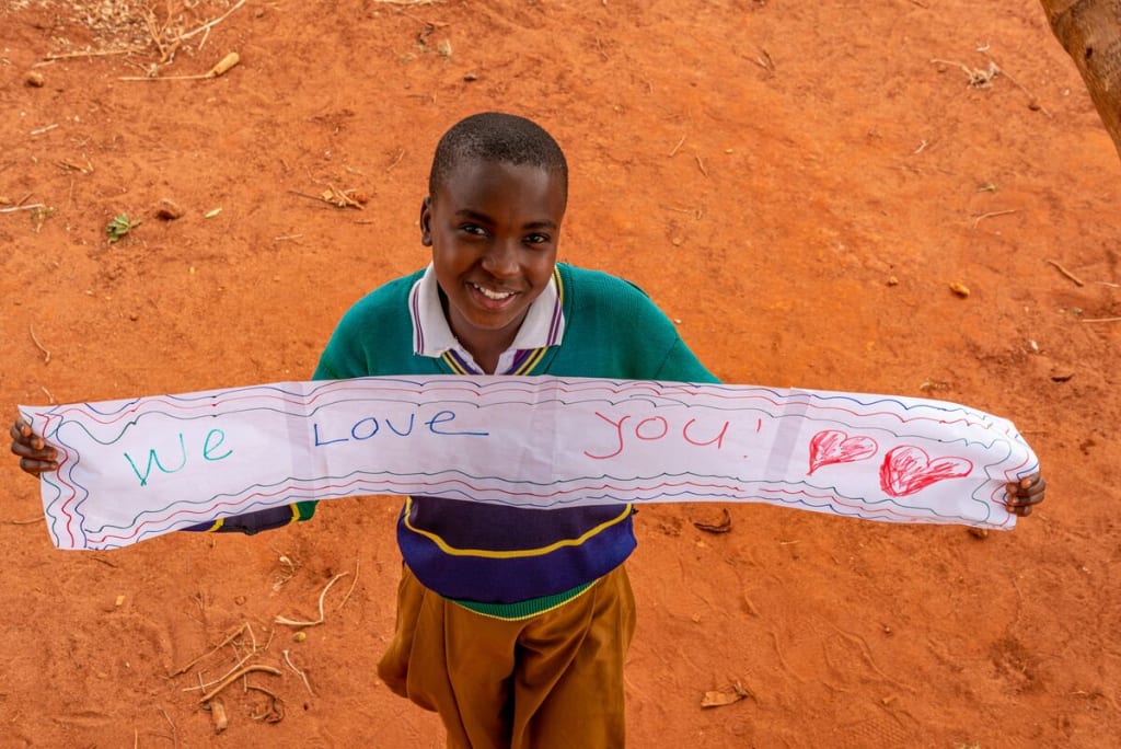 A girl wearing a green sweater holds a long sign that says,"We love you!"