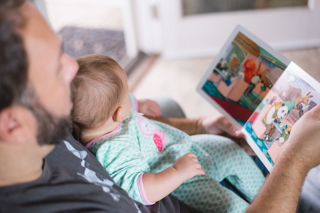 A man reading a picture book to an infant.