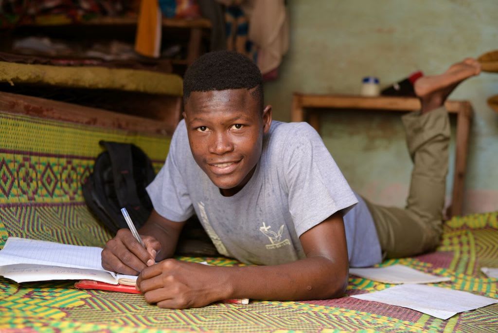 Abdoul lays on the floor of his home, working on homework.
