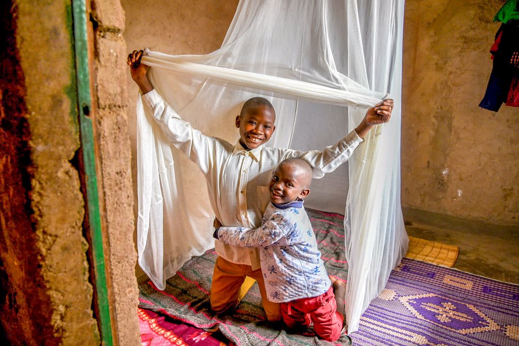 Two brothers smile under their mosquito net and bed