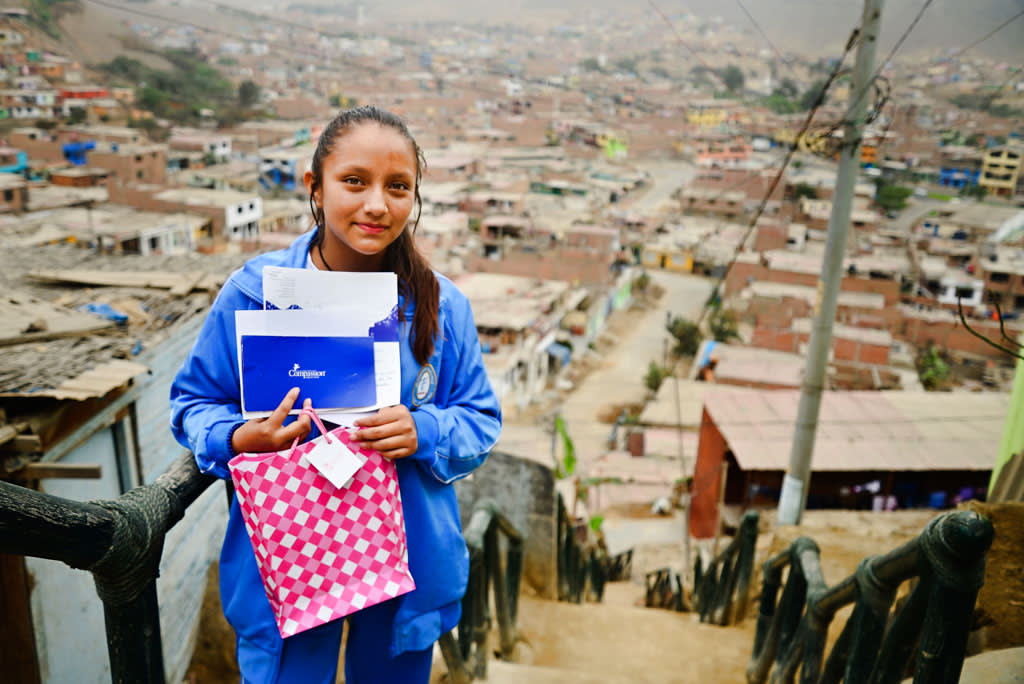 A girl stands at the top of a set of stairs overlooking city. She's holding pink bag full of paper and letters.