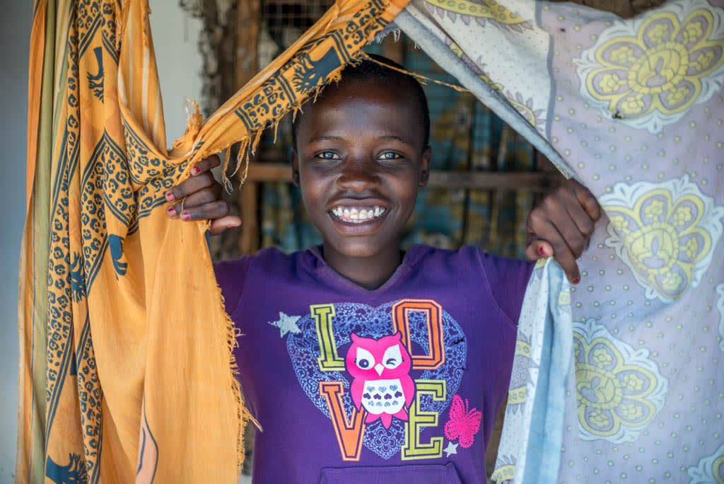 A girl holds open two curtains. Looking through it and smiling.