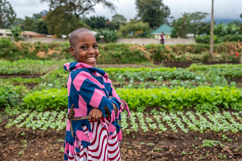 Girl wearing blue and pink stands smiling in a vegetable garden filled with seedlings