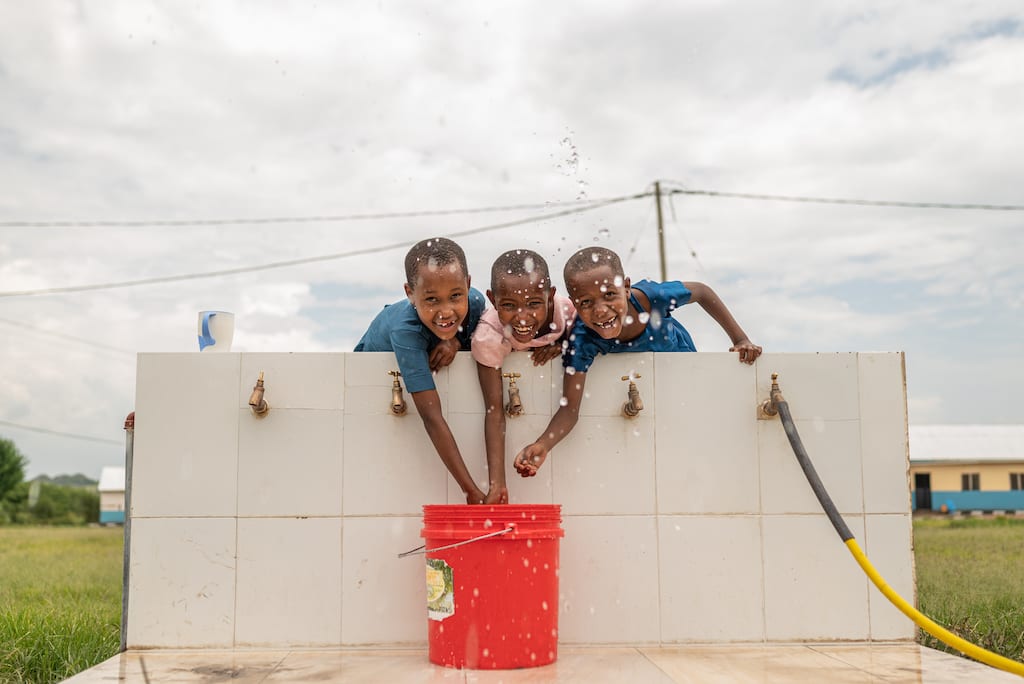 Three children are at the church's water faucets playfully splashing water out of a bucket.