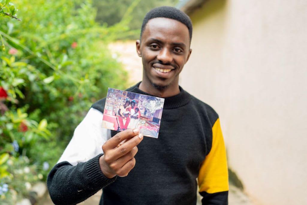 Christian smiles and holds up a printed photograph of his father holding him as a baby.