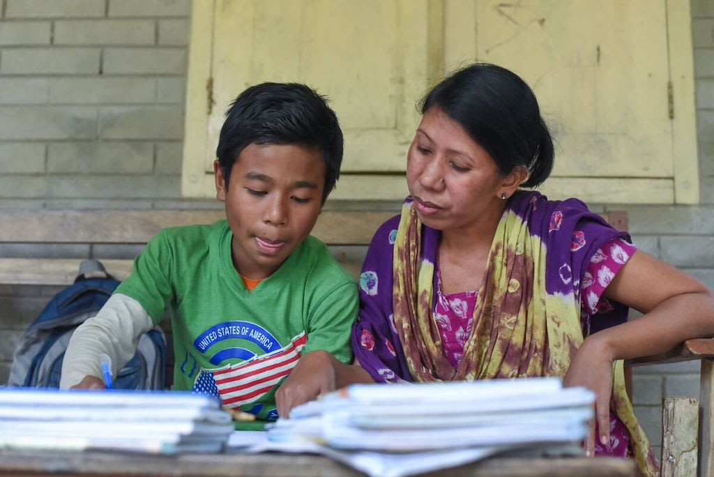 Woochang and his mother sit at a table doing schoolwork.