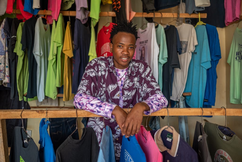 Arnold stands in a shop with colourful hanging clothes surrounding him.