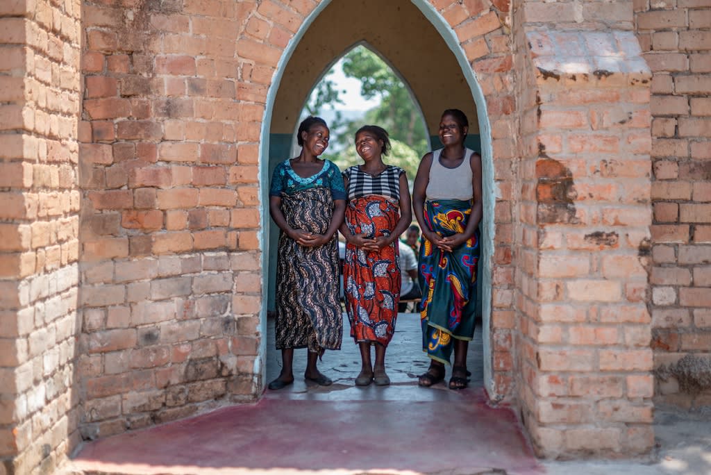 Three pregnant moms smile and pose in a brick doorway.