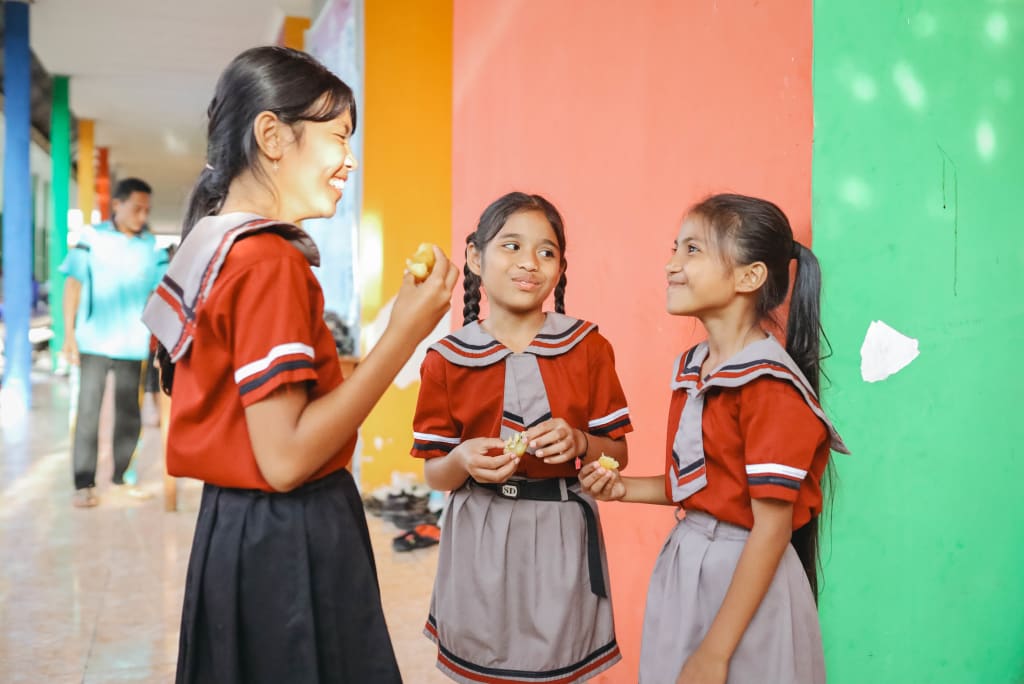 Three girls in red uniforms stand laughing together in front of a colourful wall.
