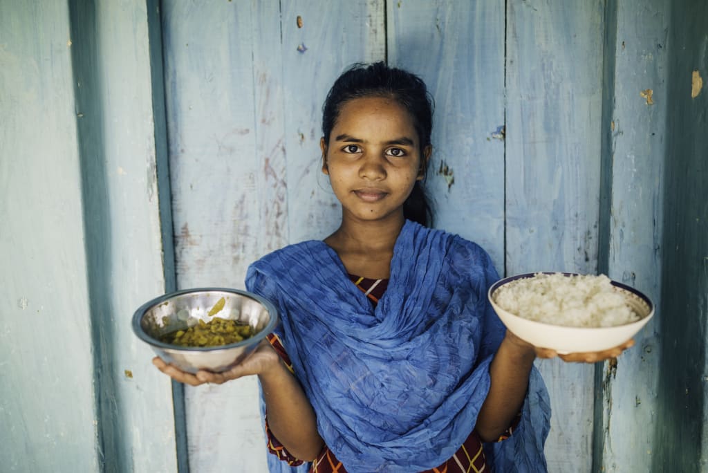 A girl in blue holds up two plates of food.