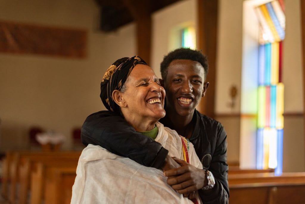 An Ethiopian boy embraces his grandmother. They are sitting in a church sanctuary.