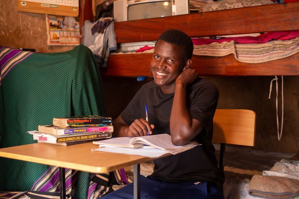 A teen boy sits at a desk in his home doing homework.