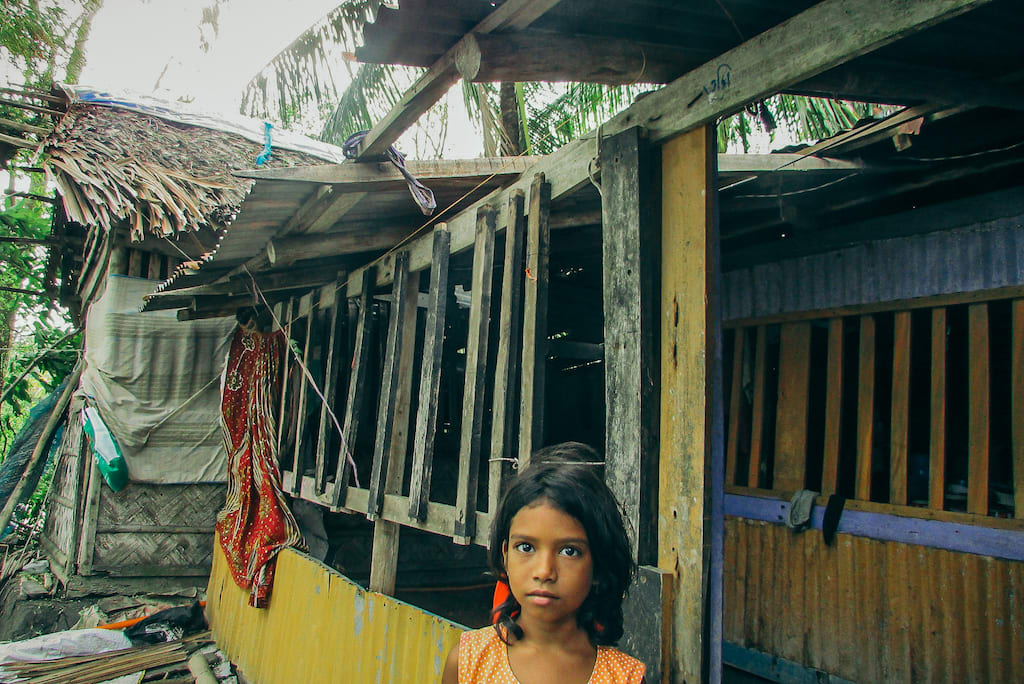 A young girl stands in front of her home. The roof was damaged in the storm.