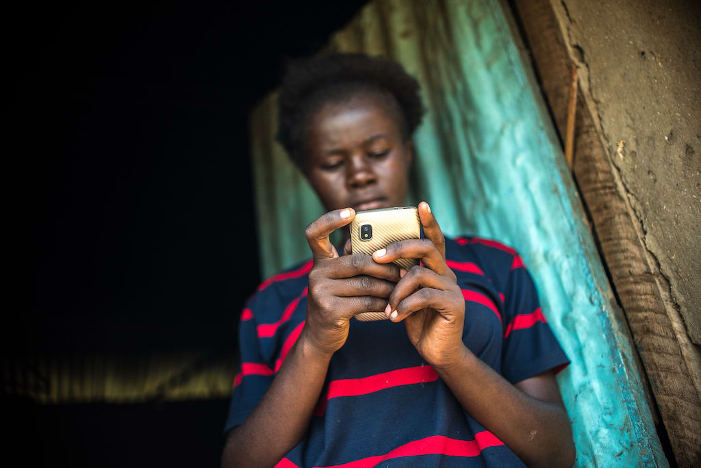 A young Kenyan girl looks down at a mobile phone.
