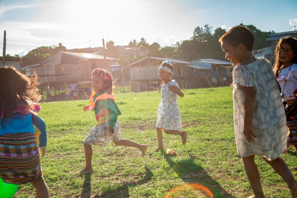 Children of the Shawi tribe run in a field, wearing their colourful traditional clothing.