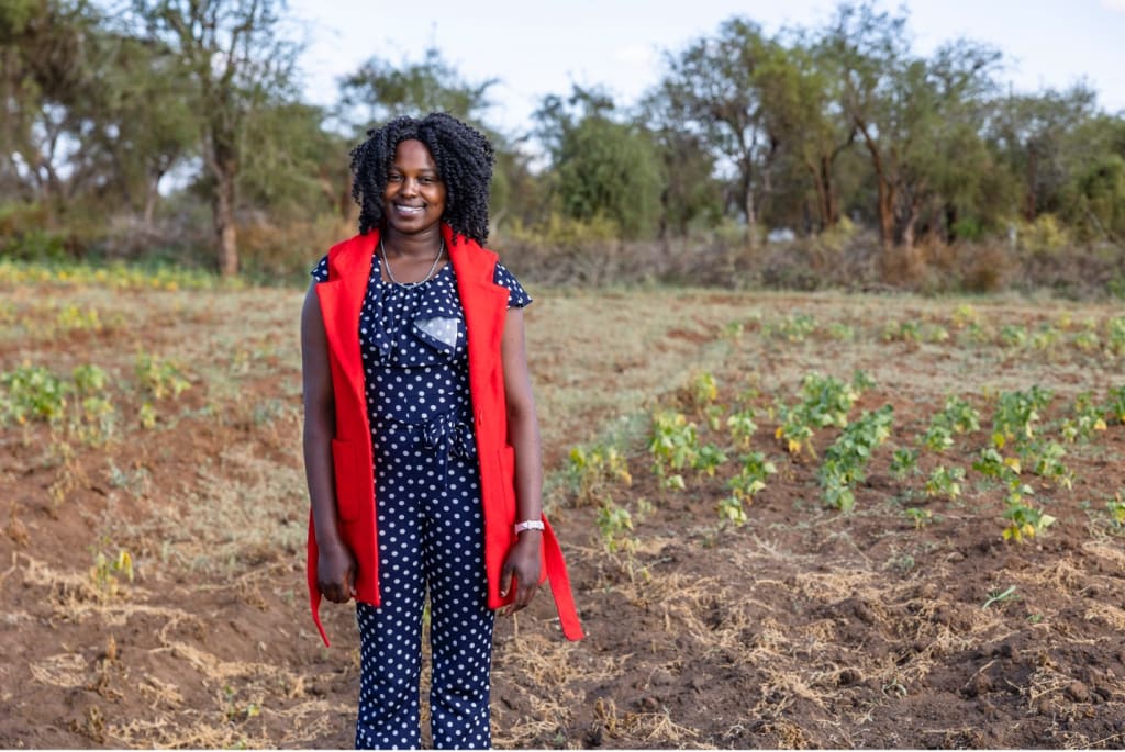 Janet, wearing polka dots and red vest, stands in a field with a smile.