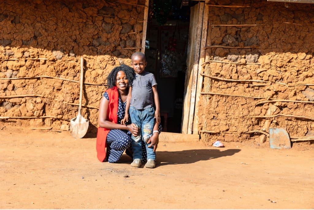 Janet has her arm around her son. They stand in front of their home.