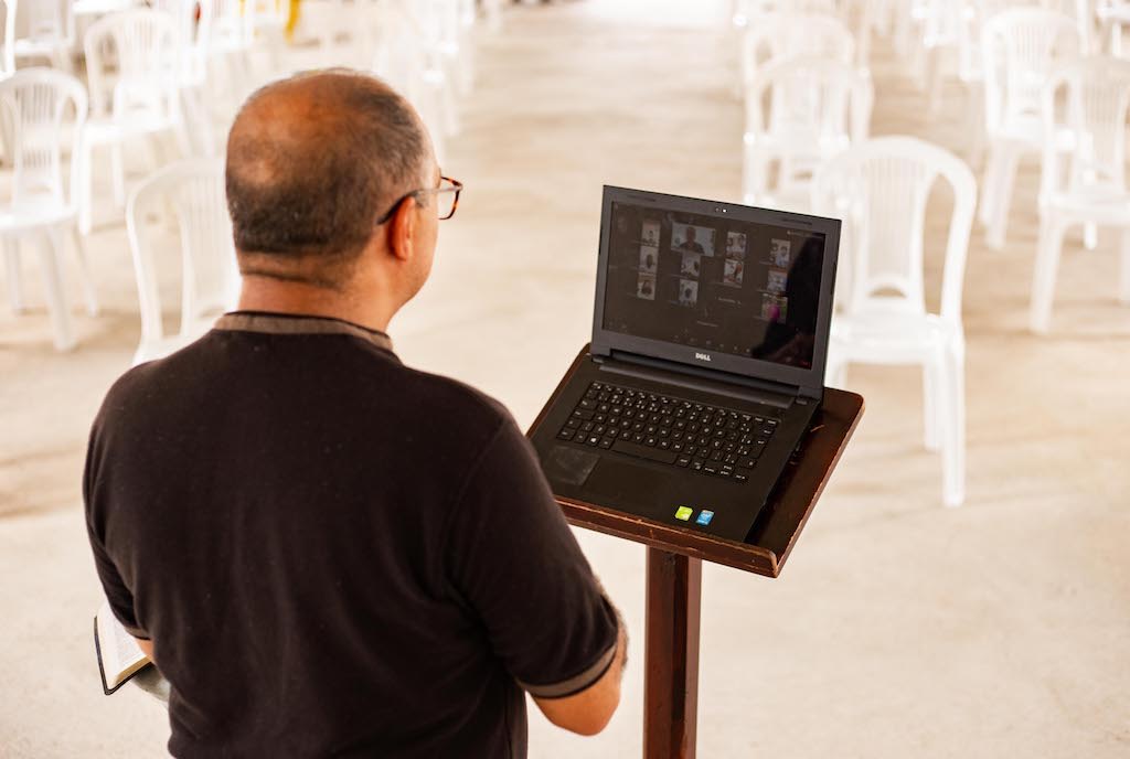 A pastor preaches to a Zoom call on a laptop.