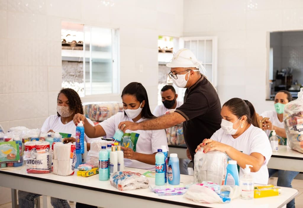 A group of adults in masks sit at a table with products