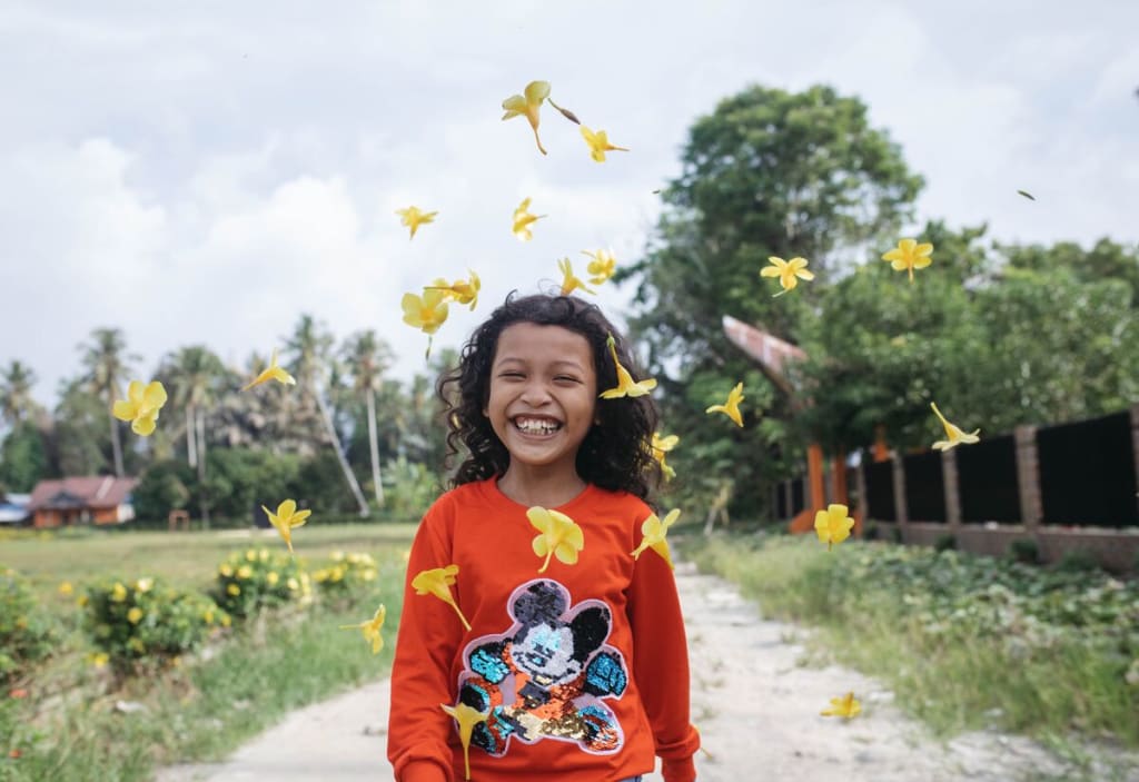 A young girl in a red sweater laughs amidst flowers in the air