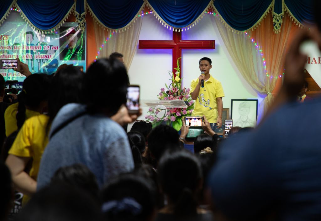 A boy in a yellow shirt holds a microphone and speaks to a group at the front of a church.