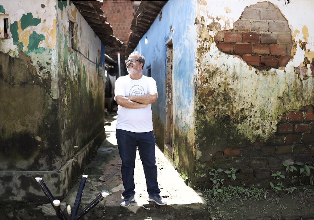 A man is wearing a white t-shirt and dark jeans and is standing in an alley.