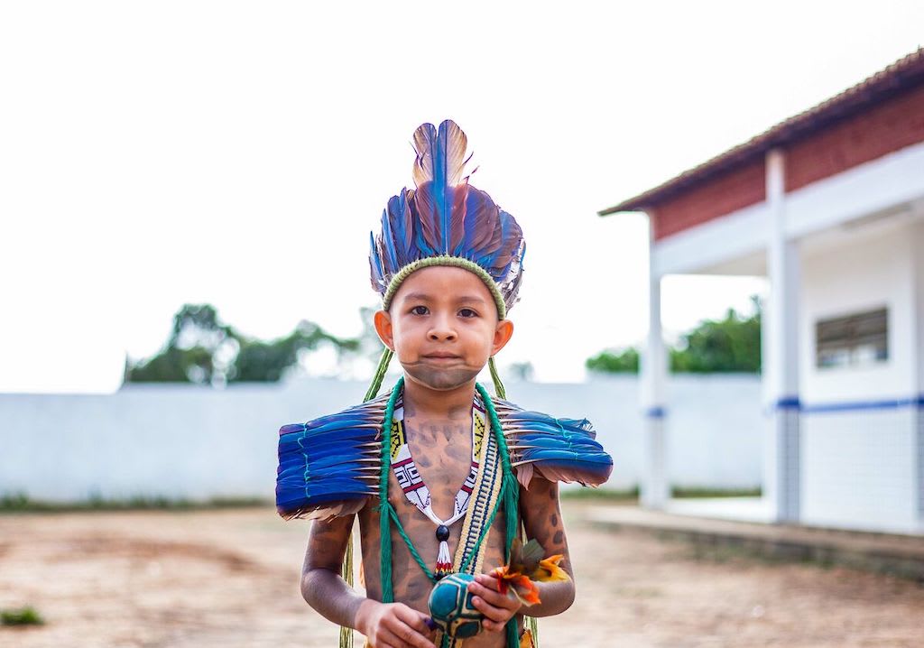 Kaio is standing outside the Compassion centre and is wearing a traditional Guajajara outfit. He is also holding a rattle. His face and body are painted with traditional designs.