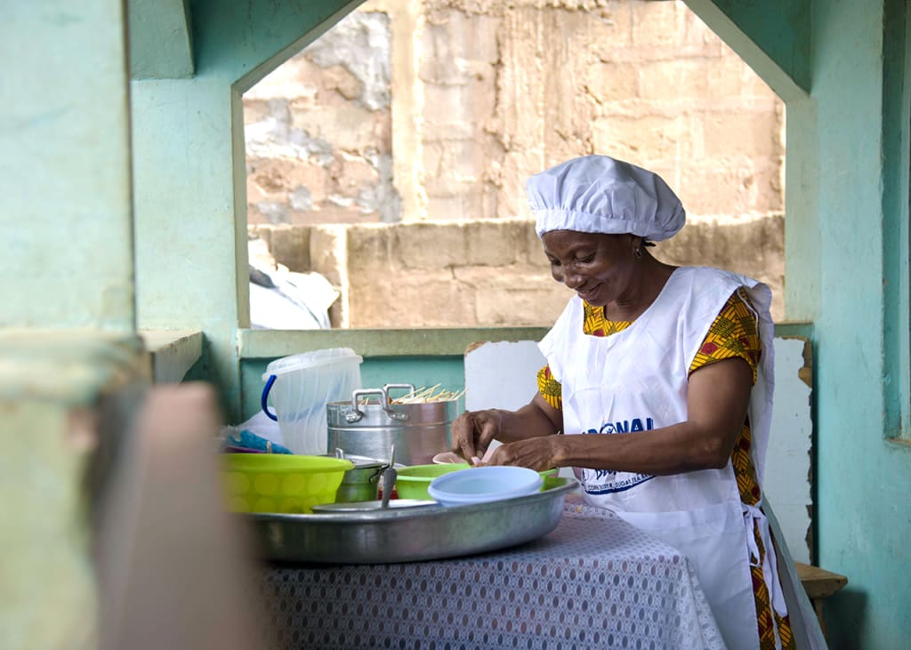 A woman cooking food, wearing an apron and chef hat.