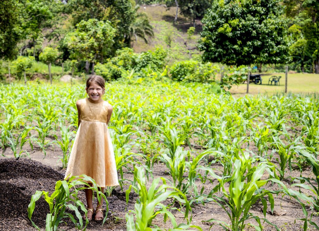 girl wearing a golden fress stands in a field smiling