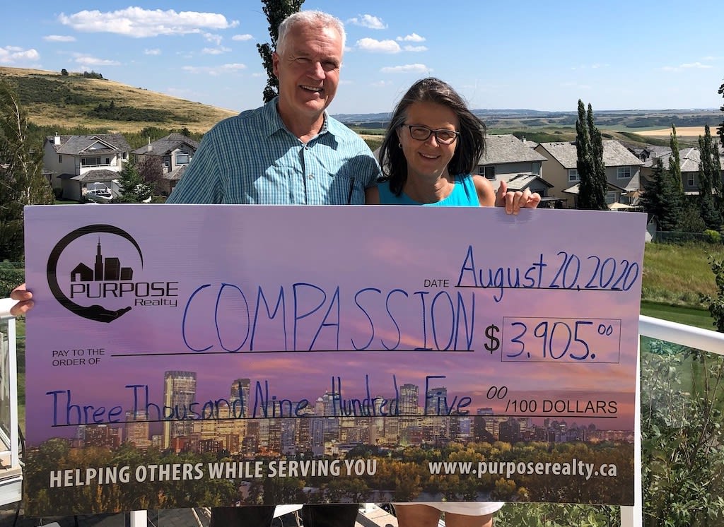 A couple holds a large cardboard cheque made out to "Compassion".