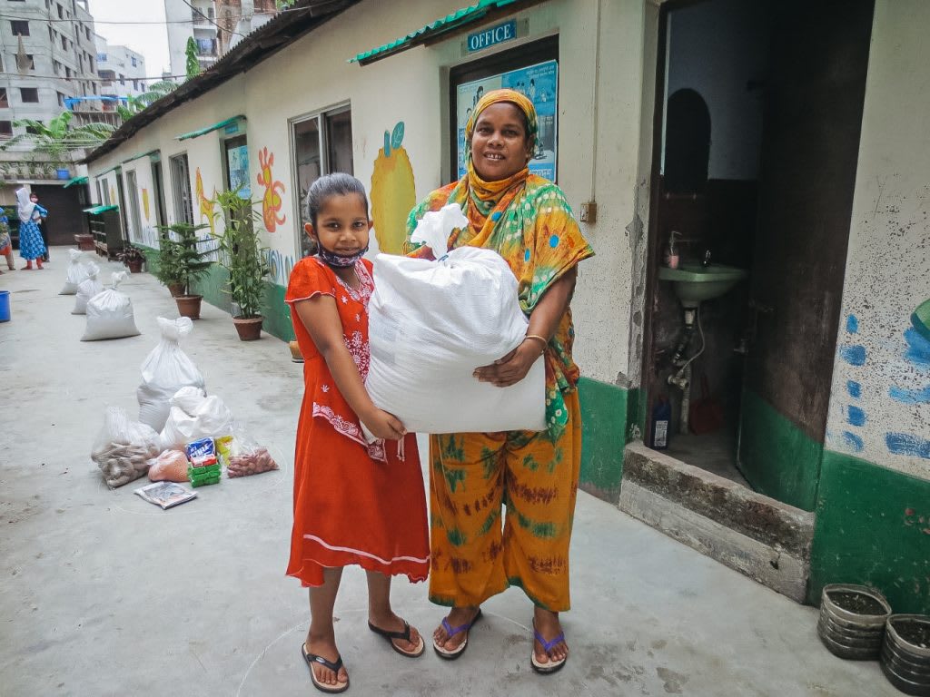 A mother and daughter hold a large white bag filled with food supplies