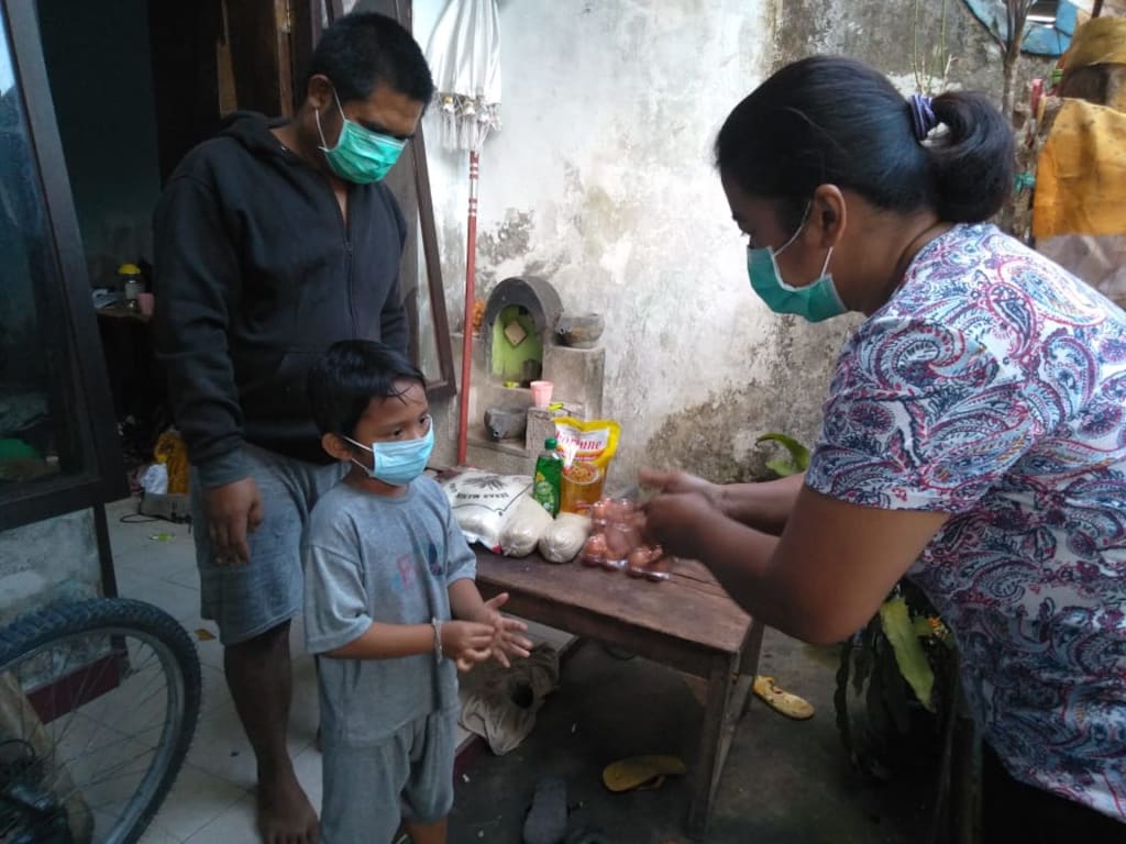A Compassion staff shows a young boy how to wash his hands effectively. Both are wearing masks.