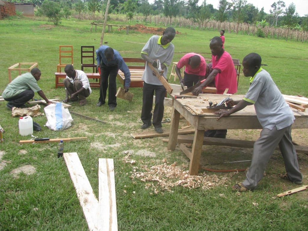 Men work with saws and other tools as they build chairs and tables