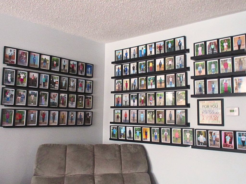 A picture of 2 walls with 101 sponsored kids photos on the walls. There is a beige couch in front of the photos.