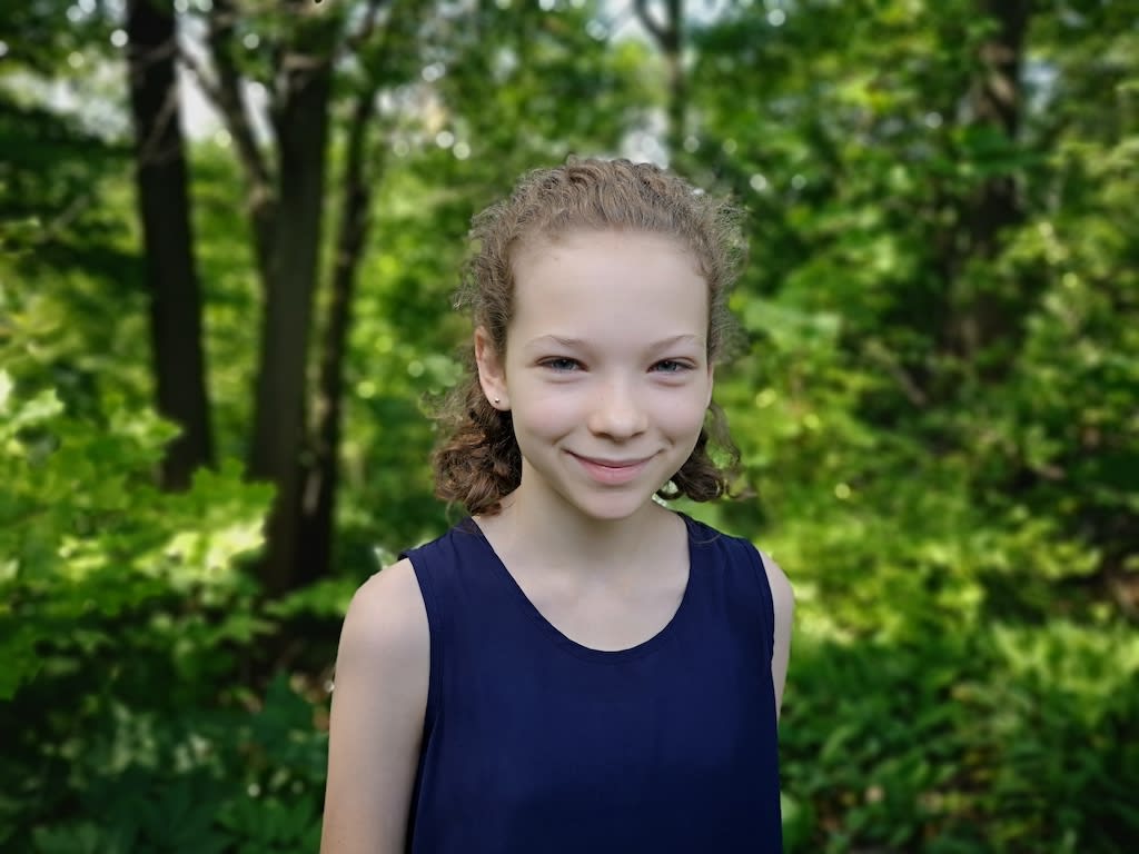 A portrait of Junia in a forest wearing a navy blue top.