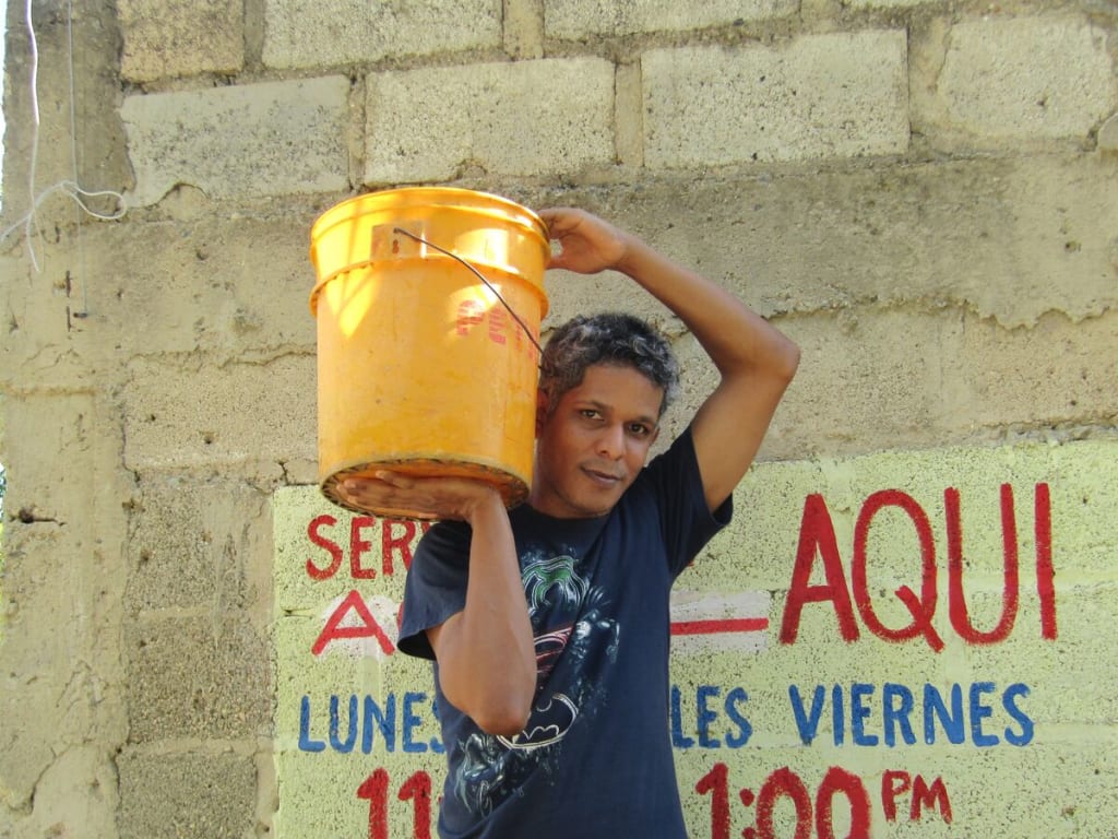 A man in a blue shirt holds a yellow bucket on his shoulder.