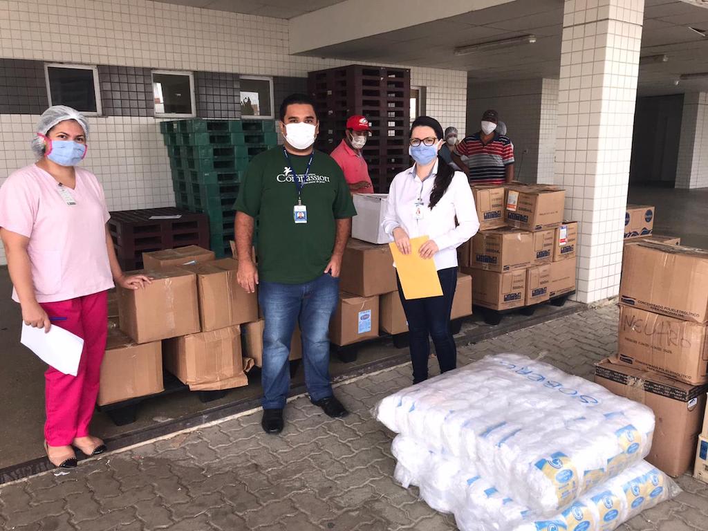 Compassion staff and hospital staff stand together outside the hospital with boxes of donated supplies. All are wearing masks.