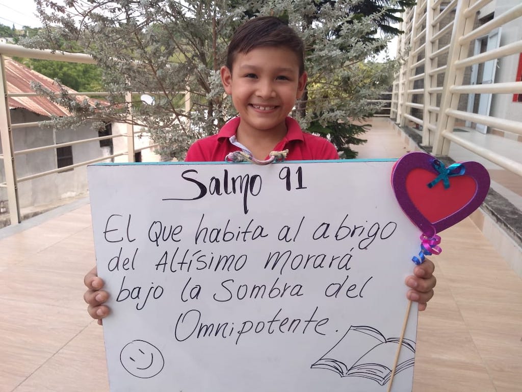 A boy holding a poster with Psalm 91:1 written on it in Spanish