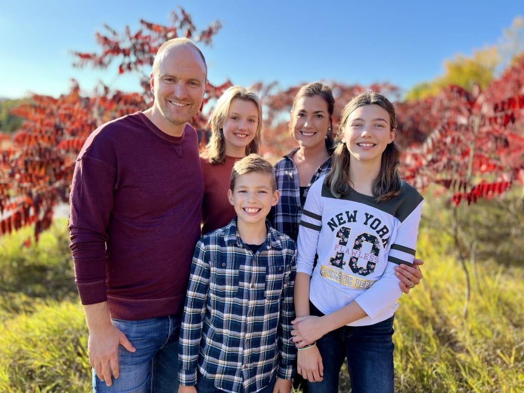 Family of five stands in front of colourful autumn trees. Ian Ardill and his family.