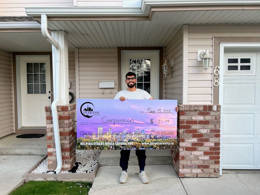 A man stands in front of his house with a large cheque.