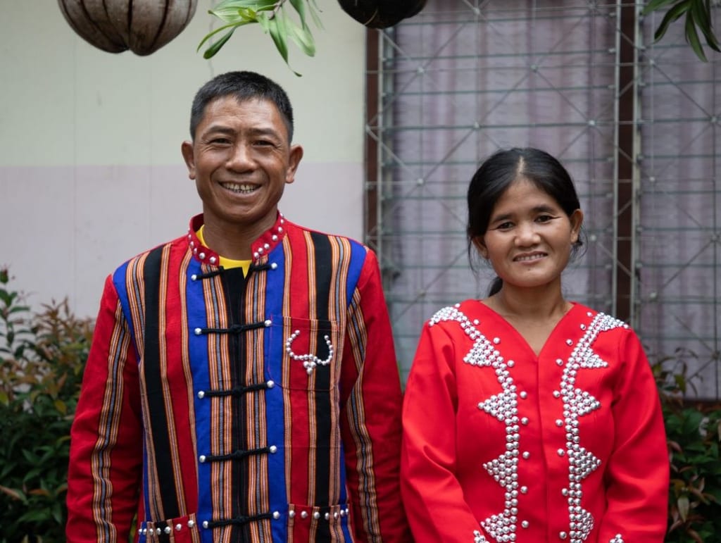 A couple smiles wearing brightly colored traditional clothing.