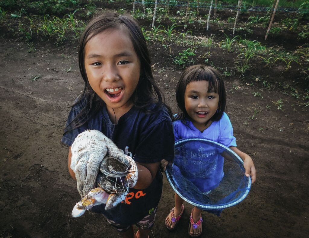 Meisy and her little sister look up at the camera holding fish and nets.
