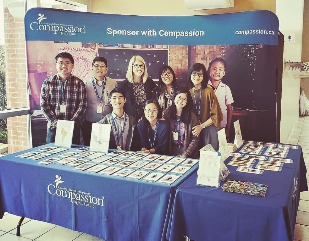 A group of people stand behind a table displaying Compassion information.