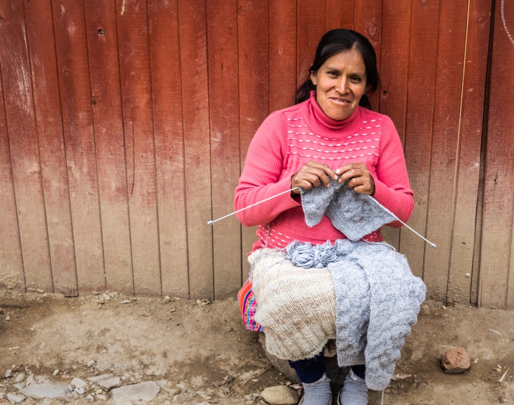 Cintia sits outside her home knitting a sweater.
