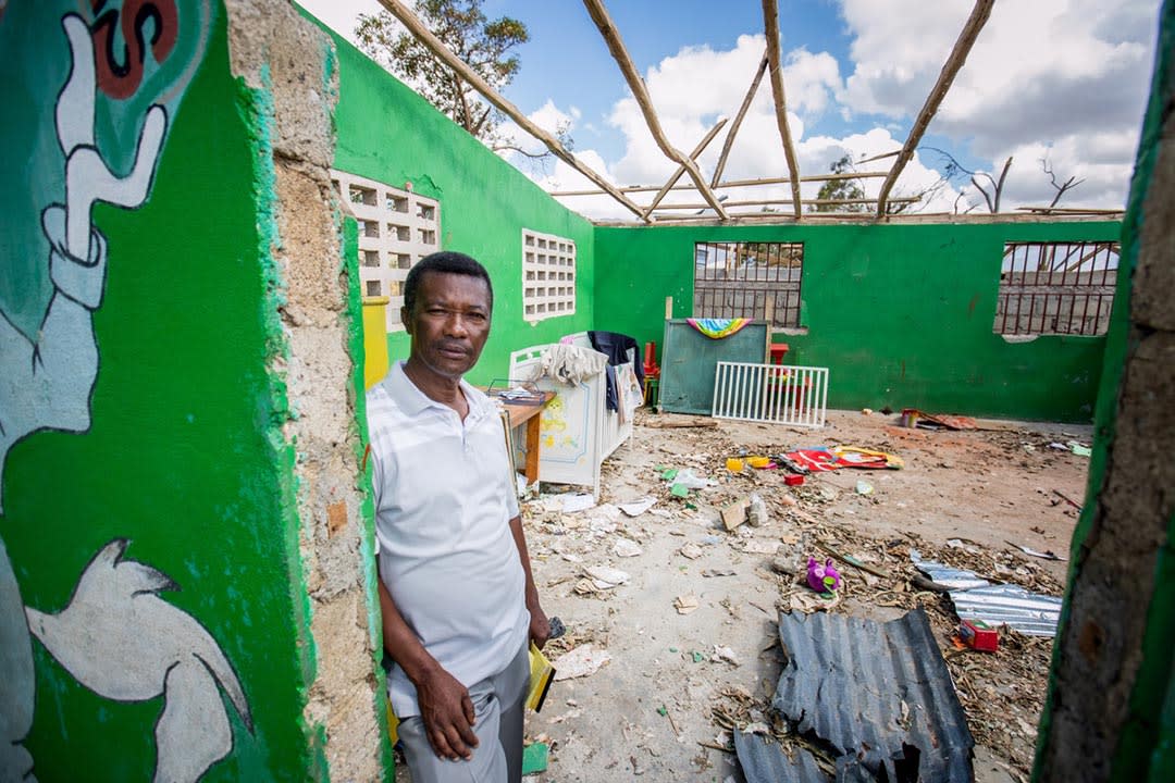 A Haitian man stands in the doorway of his storm-damaged house. Its walls are painted green, inside and out, it's roof is missing and the interior is strewn with leaves and garbage from the storm.