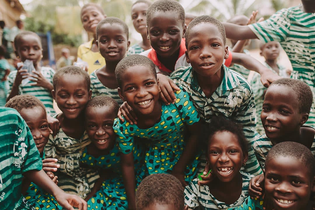 A group of children, wearing green patterned uniforms, crowd together and smile at the camera.