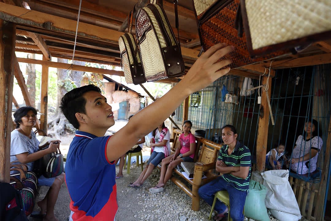 Jeric stands in an open air store front. He's inspecting hand made bags and talking to the people that sit nearby