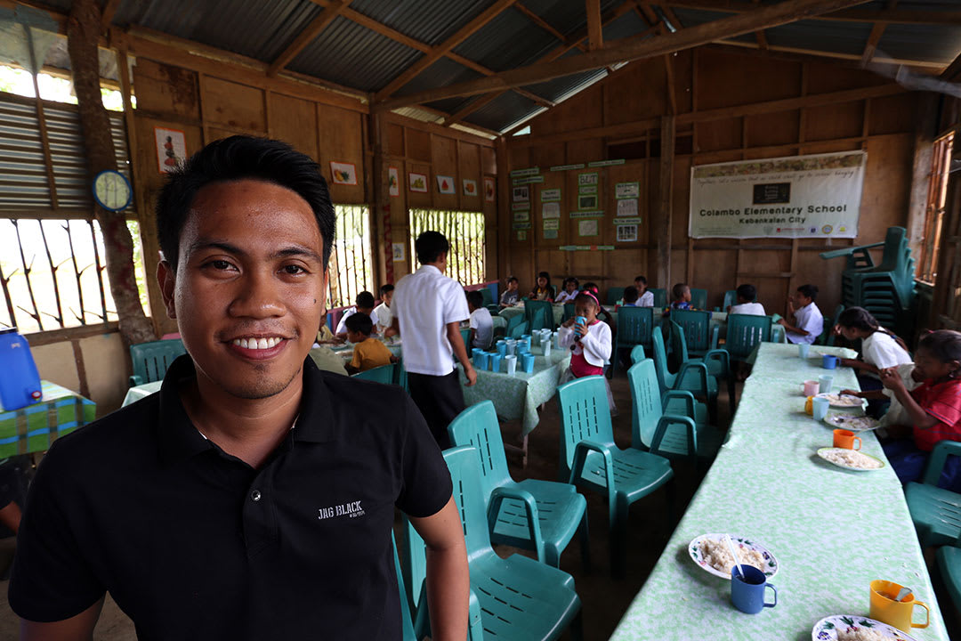Mark stands in front of his classroom in the Philippines and smiles.