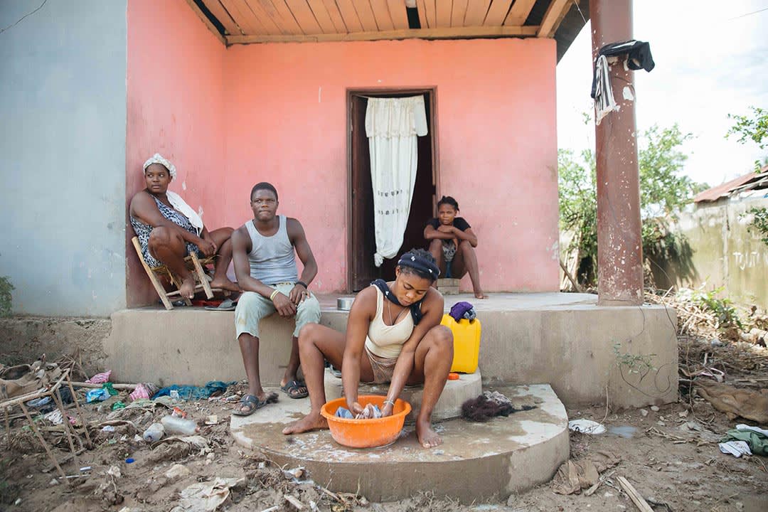 A Haitian family sits on the porch of their house surveying the damage that a recent hurricane has brought upon their neighbourhood.