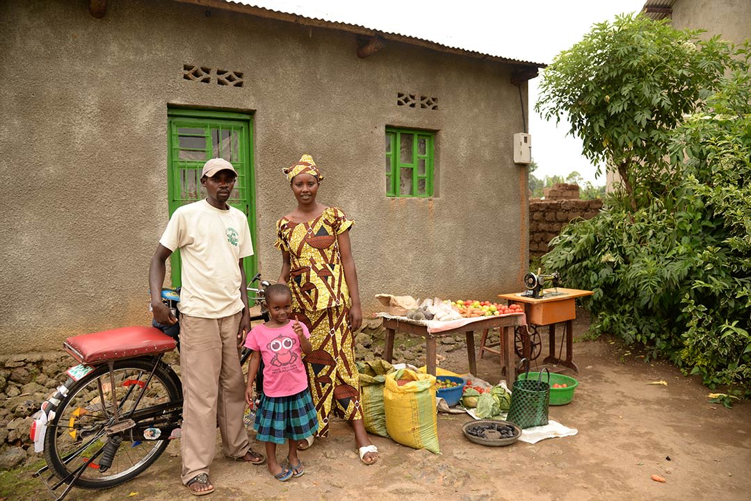 A Rwandan family stands beside the fruit stand, sewing machine and bicycle that they've used to gain an income and overcome poverty.
